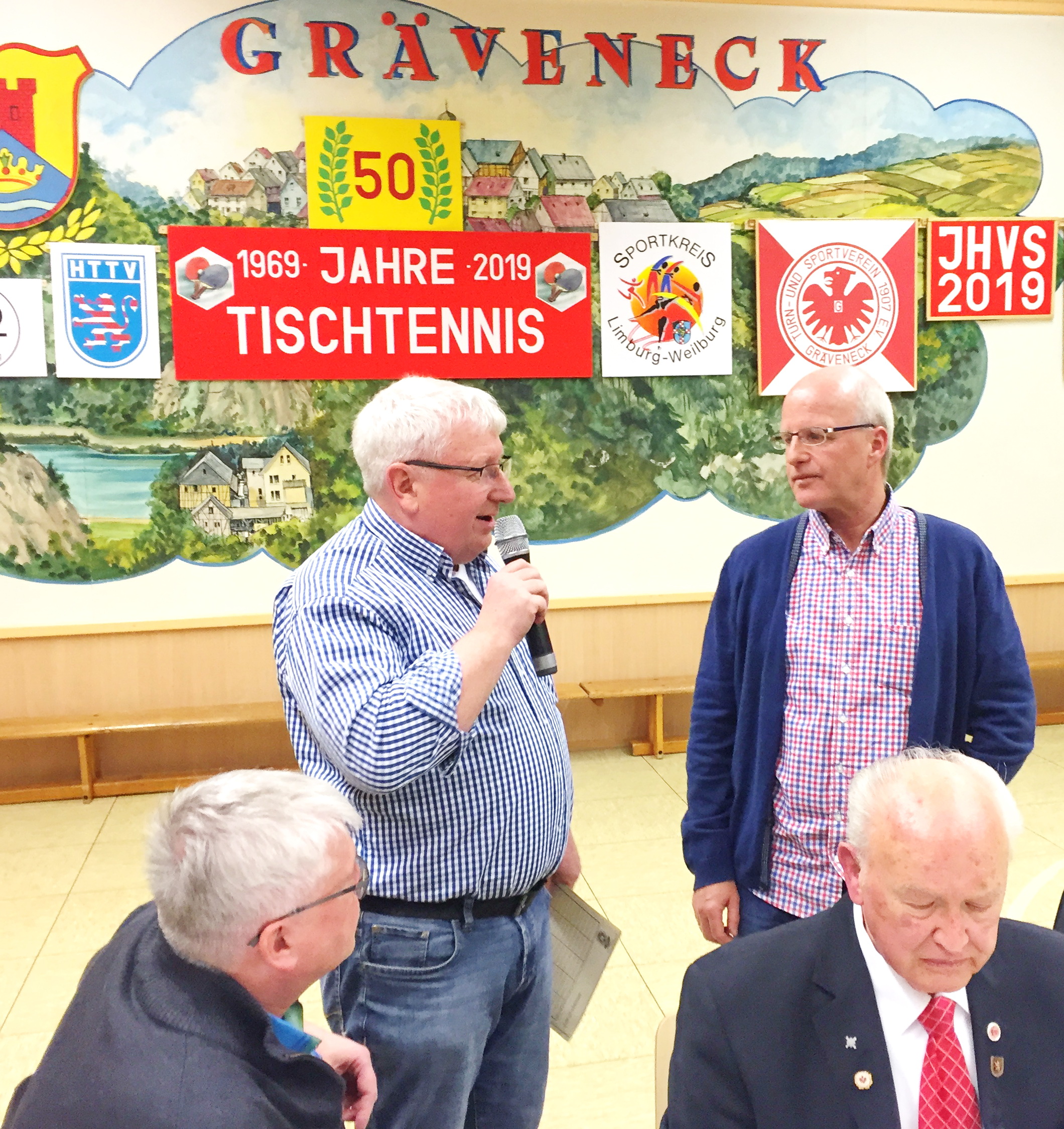 Gerd Hugo Weil (TuS Seelbach) hält Rückblick auf die vita von Gernot Lehr vor dem beeindruckenden Bühnenbild in Gräveneck. Wilfried Volz und Uli Hartmann lauschen andächtig